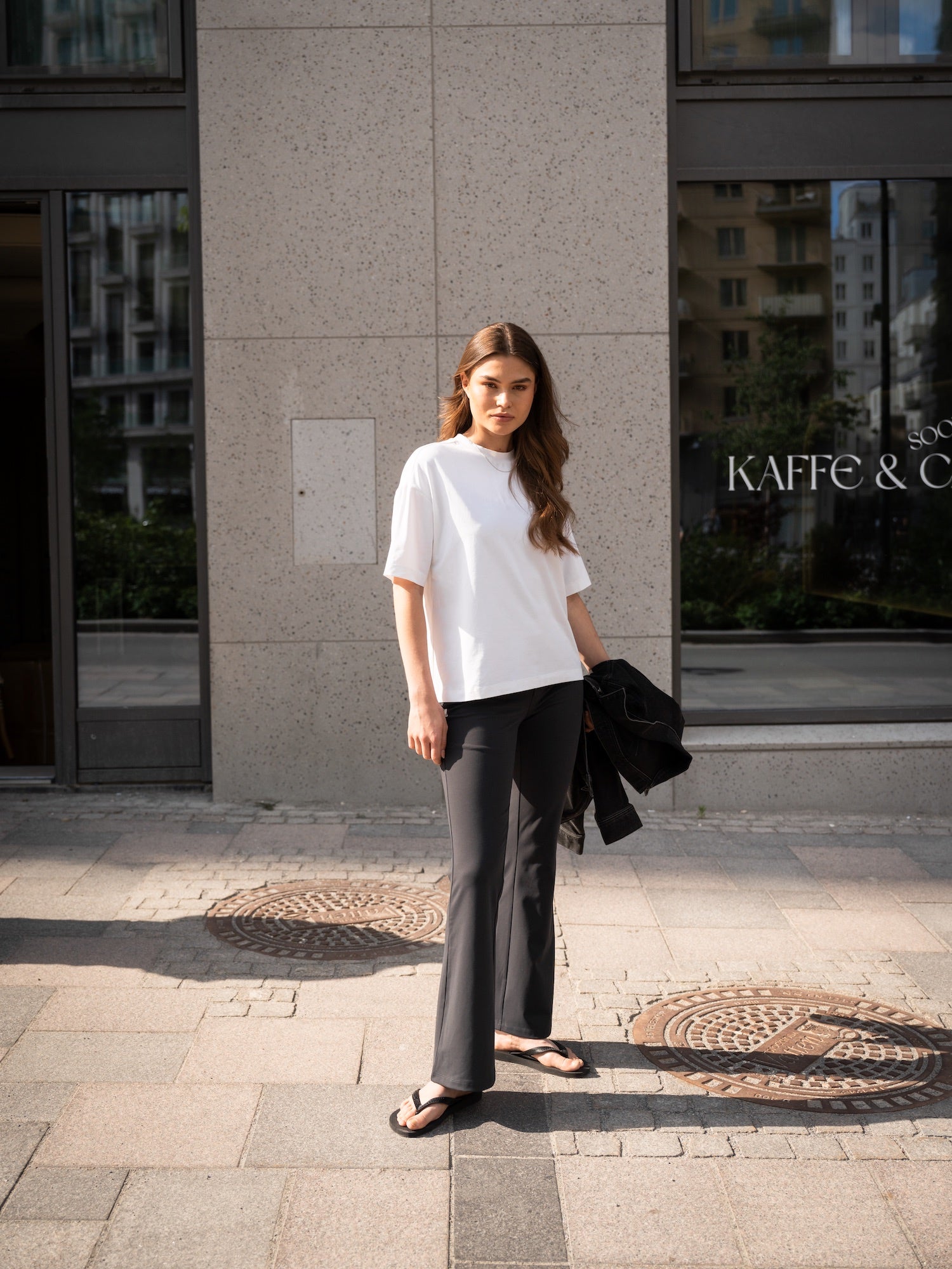 Woman wearing black Ninepine Asana Bootcut Pants with a classsic white Pima cotton t-shirt, holding a black jacket for a relaxed, polished summer outfit