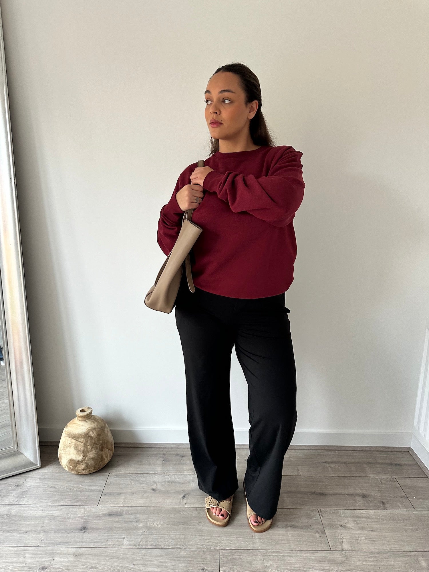 Woman wearing black Ninepine Asana Relaxed Trousers styled with a burgundy crewneck sweatshirt and beige handbag, creating a clean, minimal everyday outfit