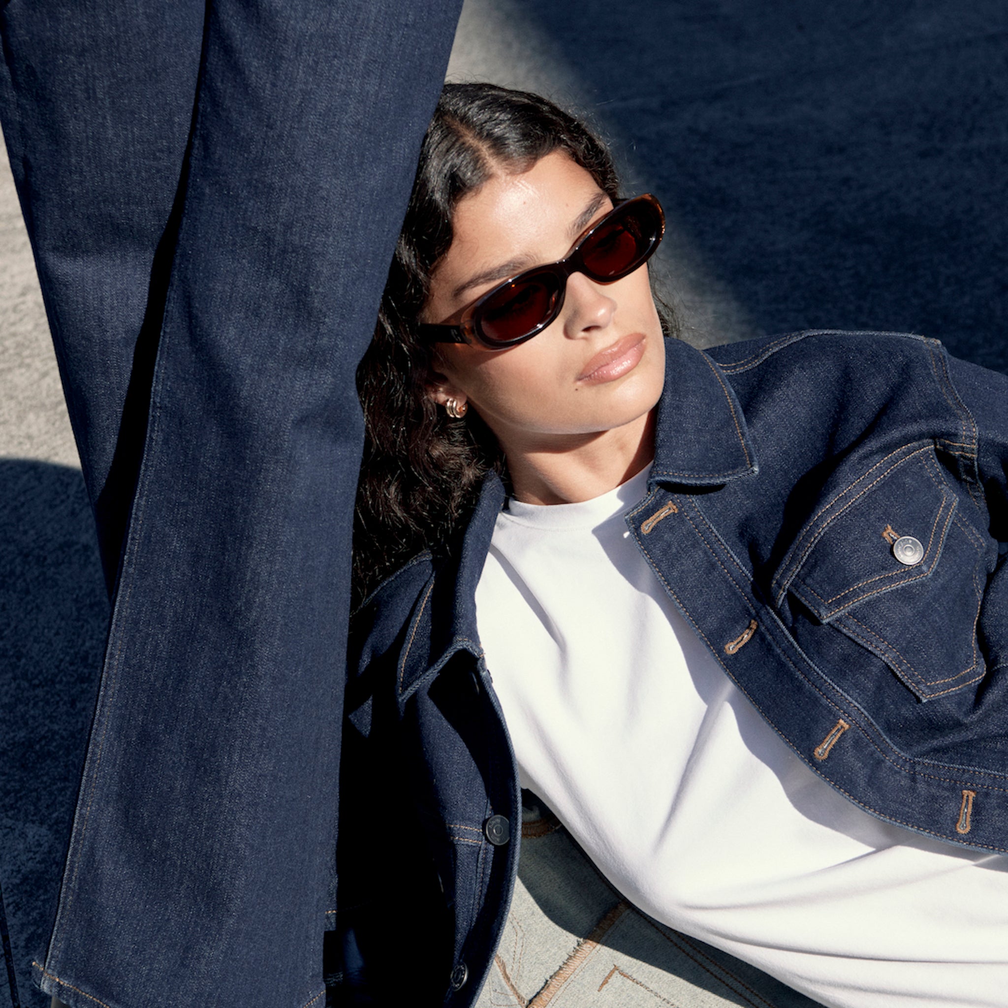 Woman wearing dark blue Ninepine ComfortDenim jeans and denim jacket lying in sun wearing sunglasses.