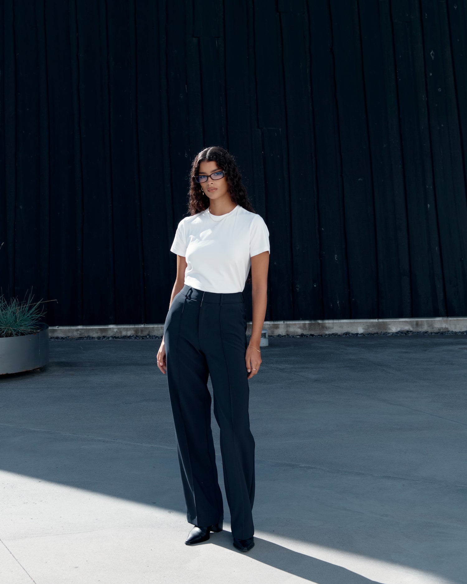 Woman wearing a white fitted Pima cotton t-shirt tucked into dark tailored trousers, styled for a clean, modern outfit with a polished silhouette